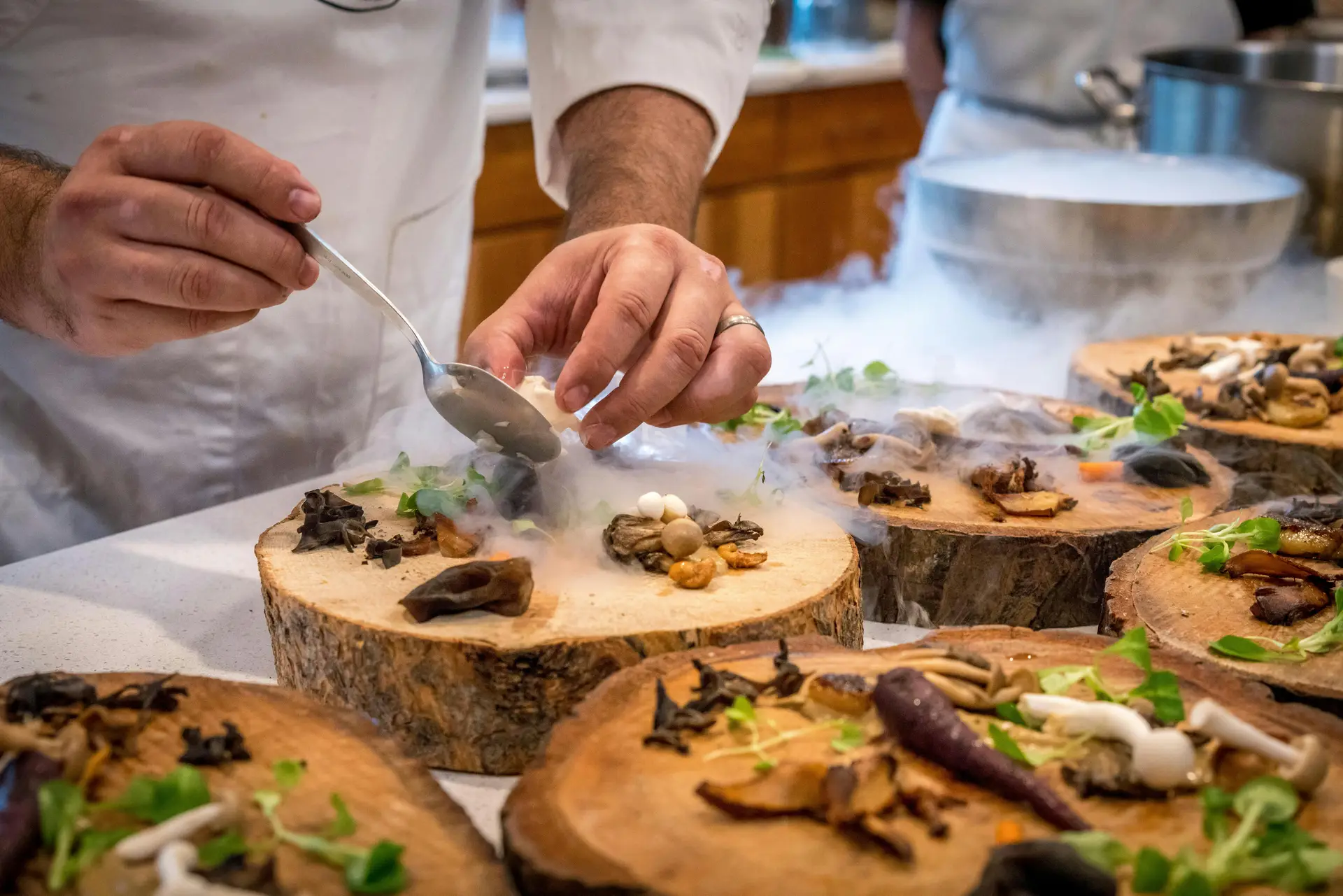 A chef artfully plating a gourmet dish with mushrooms and greens on wood slices